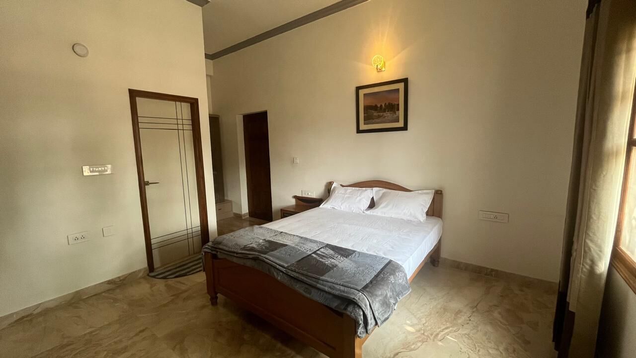 A bedroom with a bed, a nightstand, a wall-mounted light, a door, and a framed picture on the wall.