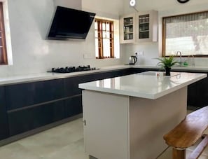 Een moderne keuken met een centraal eiland, donkere kastjes, een ingebouwd fornuis en een raam met jaloezieën.