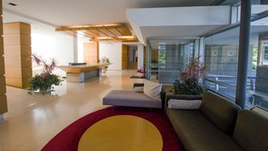 Un hall d’entrée moderne doté d’un comptoir de réception, d’espaces pour s’asseoir et de grandes fenêtres offrant une vue sur l’extérieur.