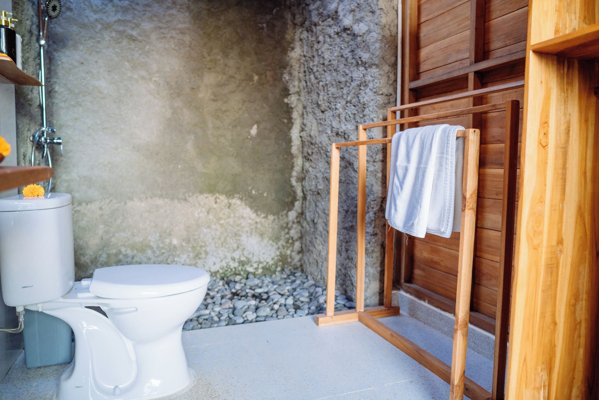 Un baño con un inodoro blanco, un toallero de madera y una zona de ducha.