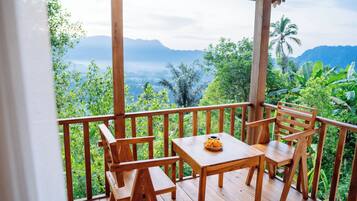 Una terraza de madera con una mesa y sillas que da a un paisaje exuberante con montañas y vegetación tropical.