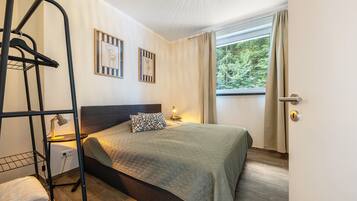 Une chambre à coucher avec un lit, une étagère fixée au mur, une fenêtre avec des rideaux et une porte.