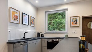 A modern kitchen with a built-in dishwasher, a coffee maker, and a window with a view of greenery. - Suites at the Historic Berghotel Theresia (Eslohe (Sauerland))