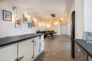 Eine moderne Küche mit einem schwarzen Kühlschrank, weißen Schränken und einer Holzarbeitsplatte. An der Wand hängen gerahmte Kunstwerke, über der Arbeitsplatte sind Pendelleuchten angebracht.
