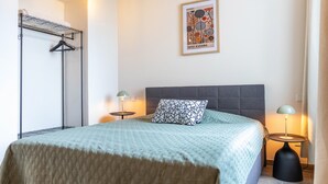 A bedroom with a bed, two bedside tables, a hanging light, a framed picture on the wall, and a coat rack. - Suites at the Historic Berghotel Theresia (Eslohe (Sauerland))