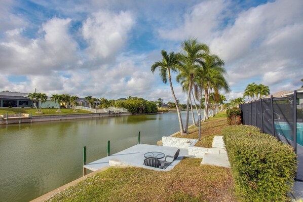 A riverside patio with a table and chairs, palm trees, and a swimming pool. - Fishing Dock & Pool: Waterfront Cape Coral Retreat (Cape Coral)