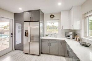 A modern kitchen with stainless steel appliances, white cabinetry, and a window overlooking a pool. - Fishing Dock & Pool: Waterfront Cape Coral Retreat (Cape Coral)