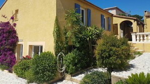 A yellow building with a tiled roof, a garden with various plants, and a stone pathway.