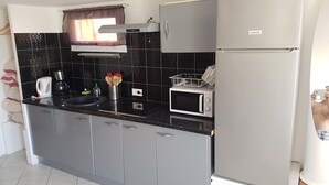 A modern kitchen with grey cabinets, a black tiled backsplash, a microwave, a kettle, and a refrigerator.