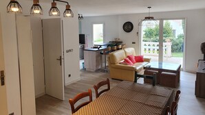 A modern living room with a dining area, a kitchen in the background, and a sliding glass door leading to a balcony.