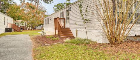 A row of mobile homes with a grassy yard and a wooden staircase leading to the entrance.