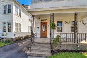 A two-story house with a front porch, a wooden door, and a small garden area with a metal railing.