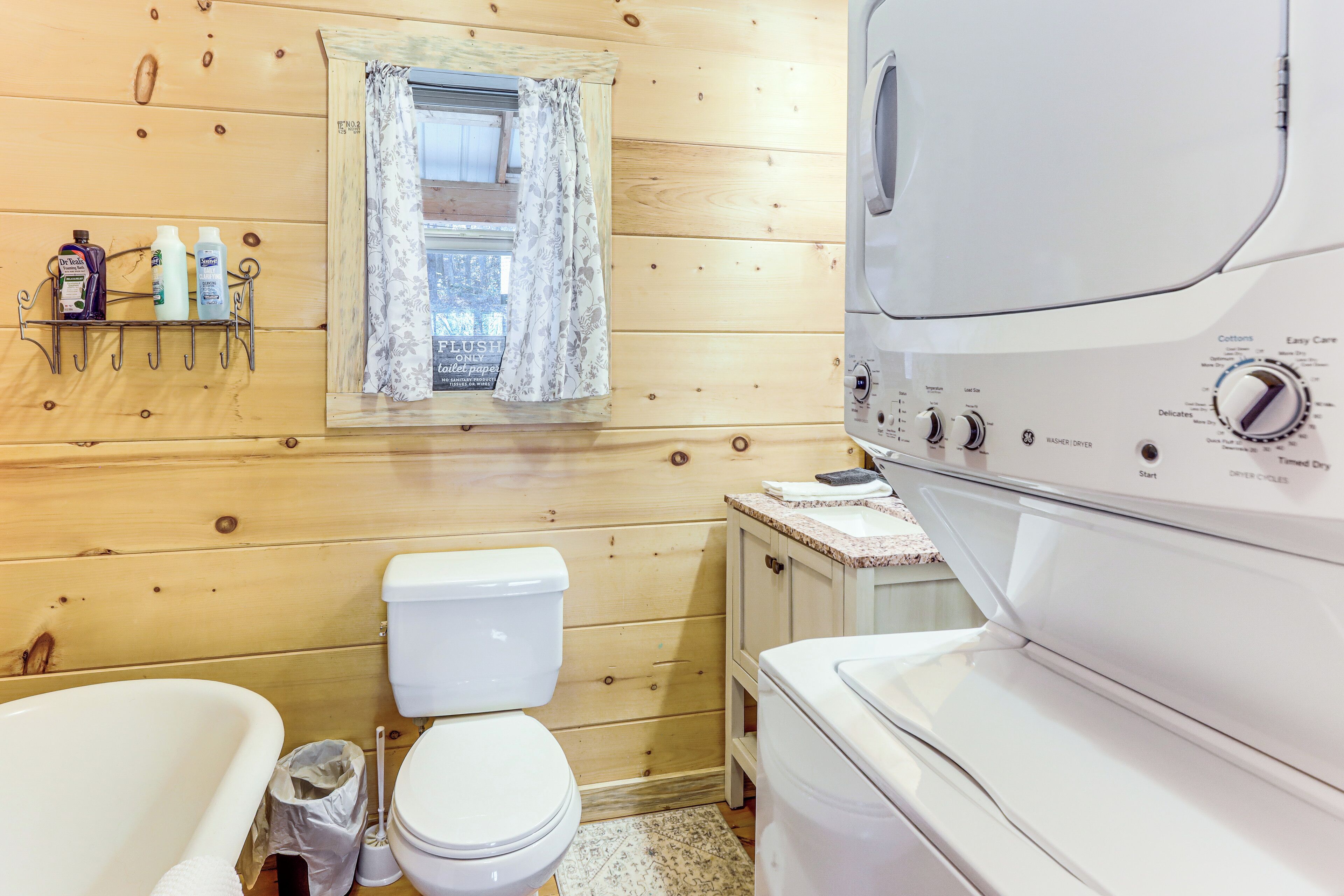 A wooden cabin bathroom with a white toilet, a bathtub, and a washing machine.