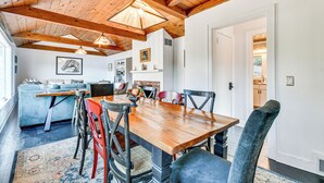 Ein Essbereich mit Holztisch, Stühlen und Teppich. Im Hintergrund ist eine Küche mit Schränken und einer Arbeitsplatte zu sehen.