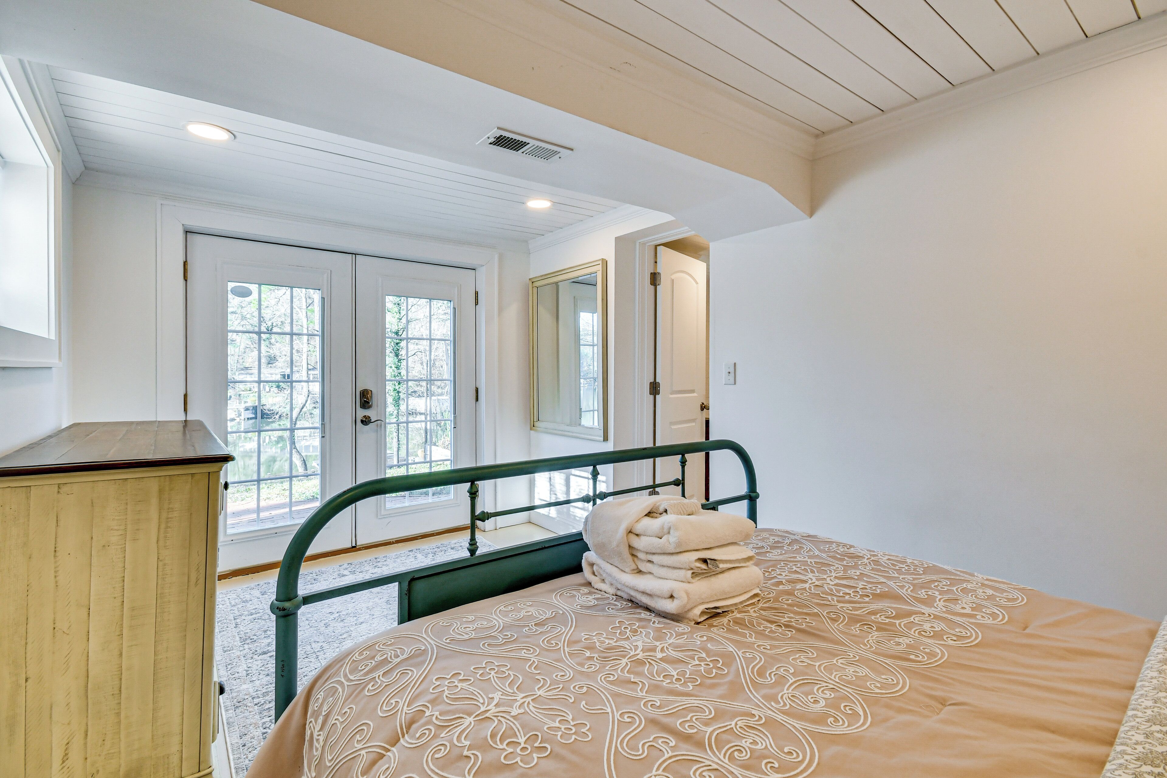 A bedroom with a bed, a wooden dresser, and a window with a view of trees.