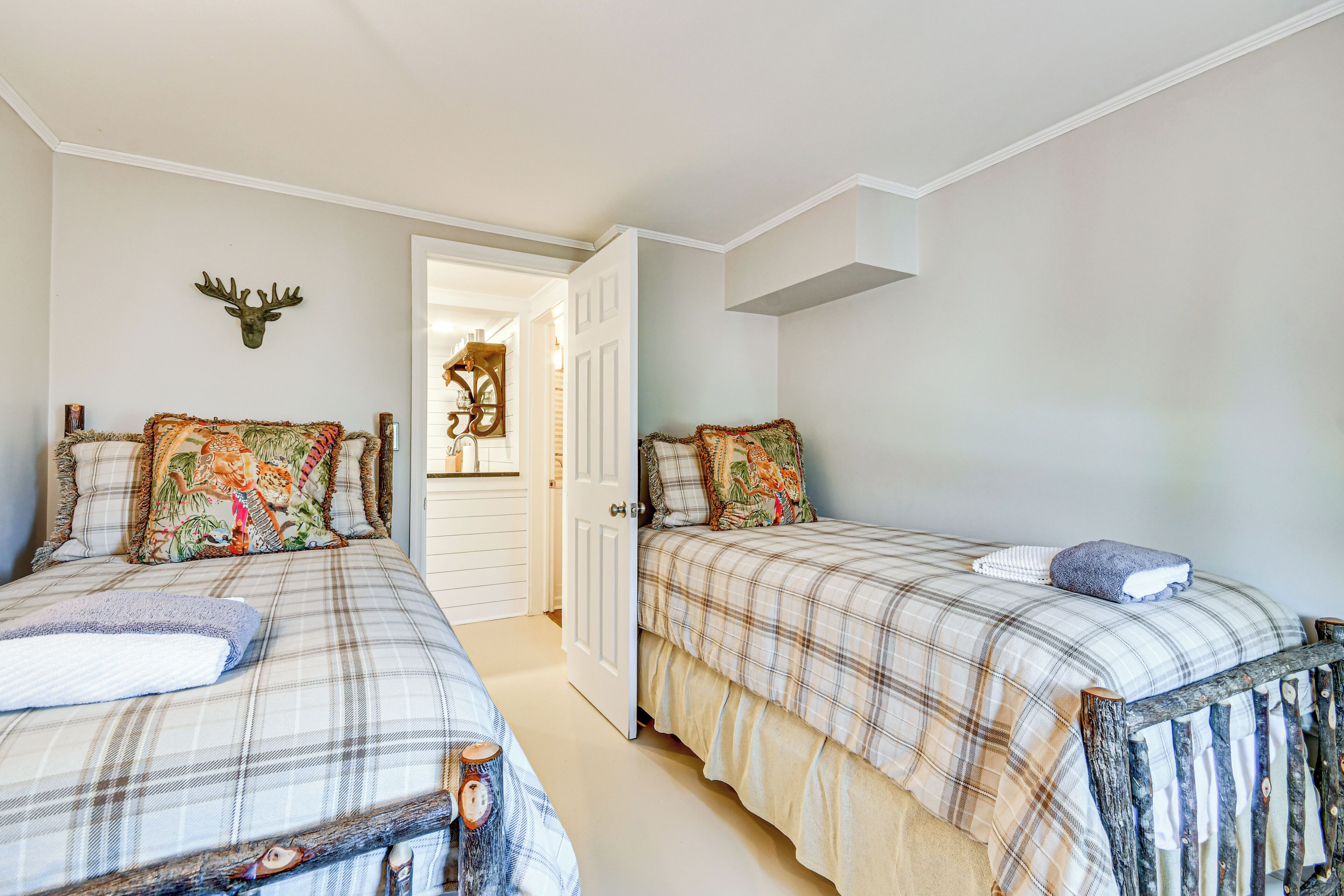 A room with two beds, each with a plaid bedspread and decorative pillows. A deer head is mounted on the wall above the beds.