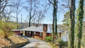 Ein rustikales Blockhaus mit einem Schotterweg, der zu einer Holztür führt, umgeben von Bäumen und einem Gewässer im Hintergrund.