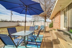 A patio with a table and chairs, a blue umbrella, and a brick house in the background. - On Route 66! Bristow Home w/ Spacious Yard (Bristow)
