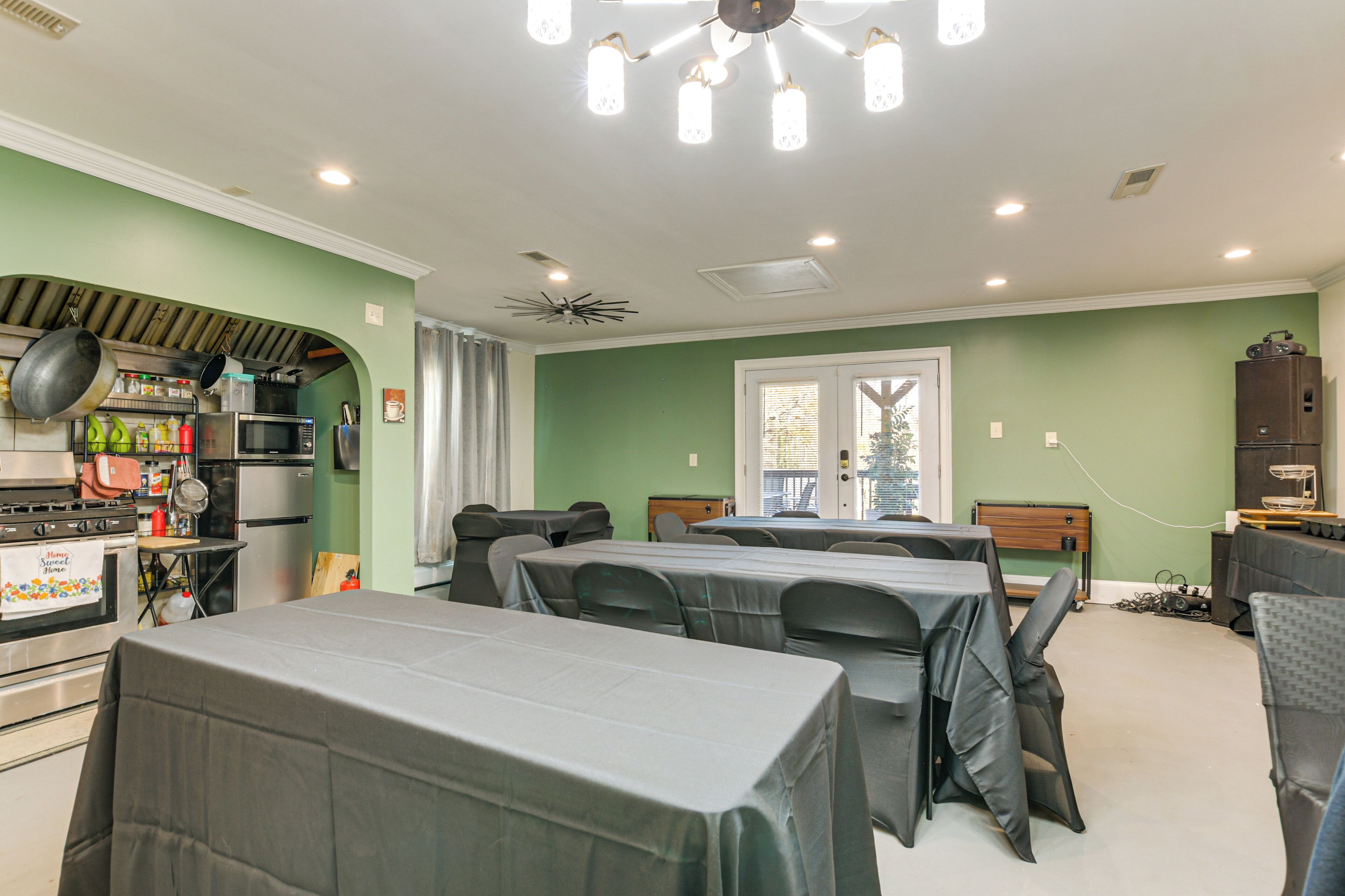 A dining area with tables and chairs, a kitchen with appliances, and a ceiling fan.