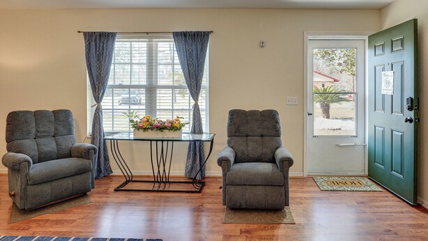 A room with two armchairs, a small table with a vase of flowers, a window with curtains, and a green door. - Close to Highway & Border: North Florida Hideaway (Jennings)