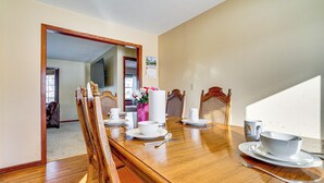 A dining room with a wooden table set for four, chairs, a vase with flowers, and a calendar on the wall. - 12 Mi to St Paul: Pet-friendly Home w/ Backyard (Cottage Grove)