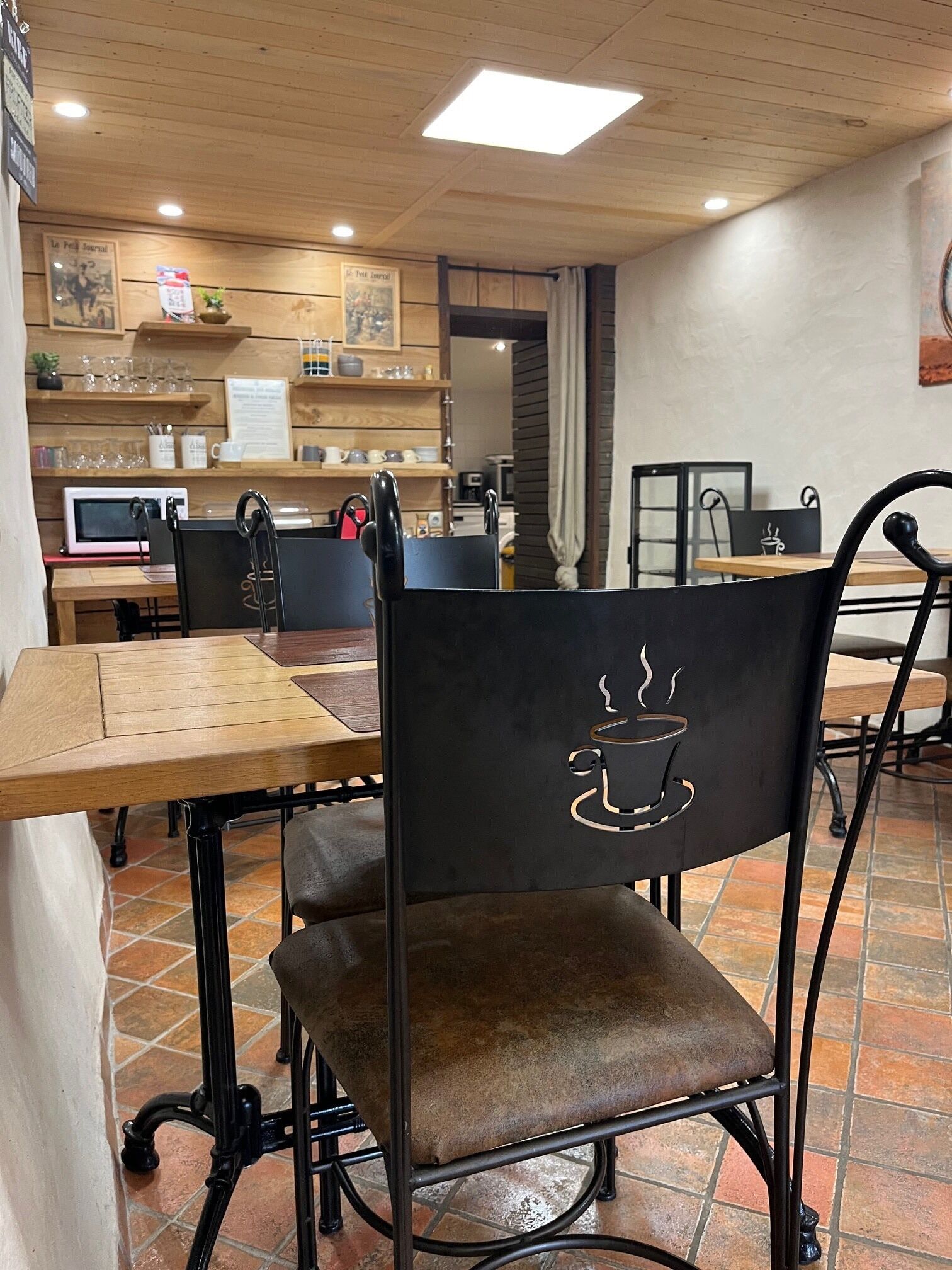 A café interior with wooden tables, black metal chairs, and a tiled floor.