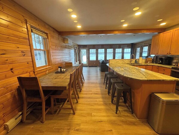 A spacious kitchen with wooden walls, a large island with bar stools, and a view through the windows.