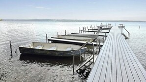 En træbro strækker sig ud i roligt vand med flere både fortøjet i enden.