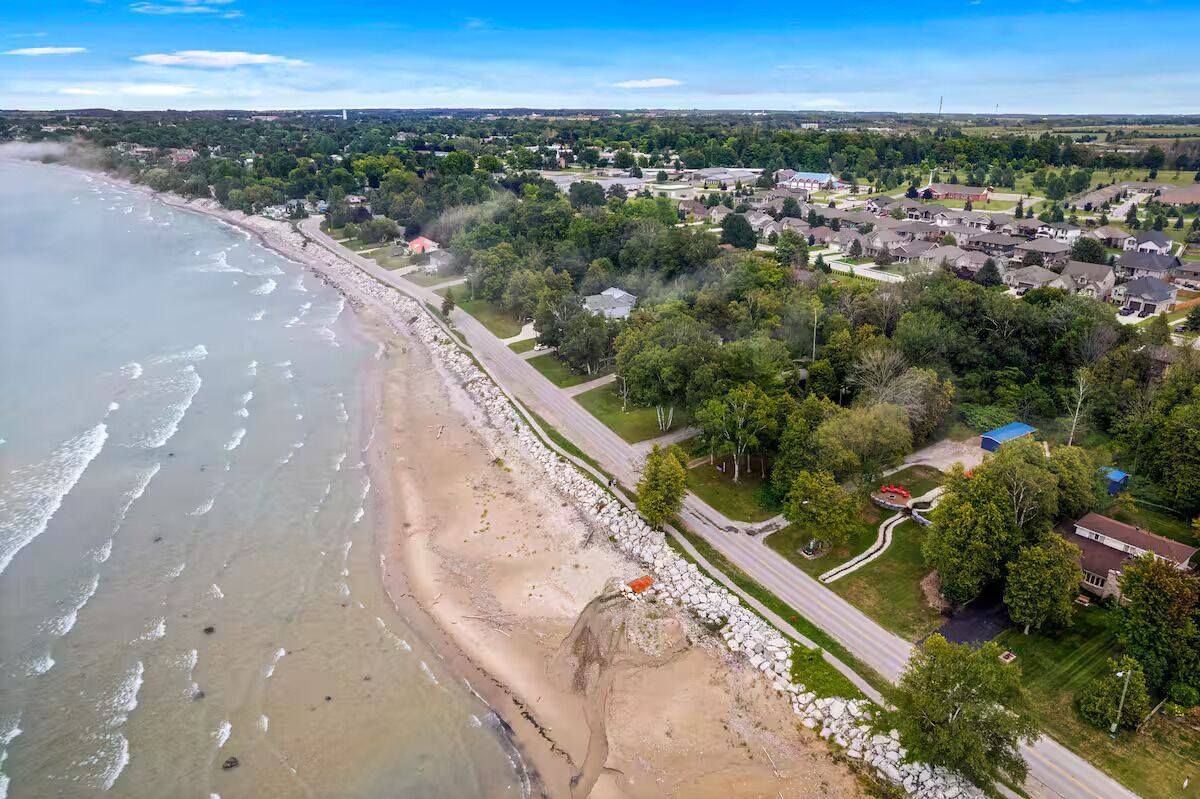 Vue aérienne d’une zone résidentielle côtière, avec des maisons, une plage et une route.