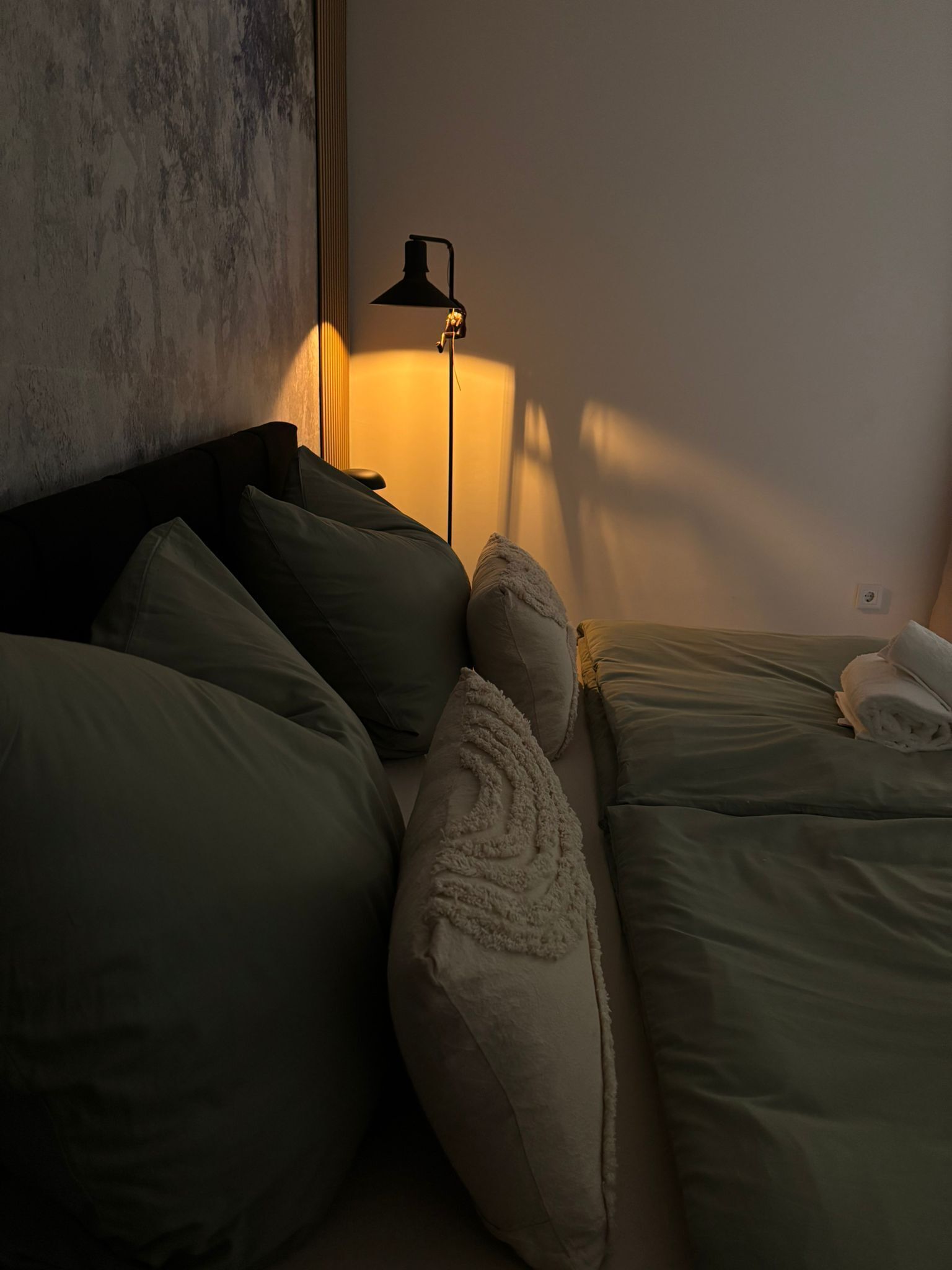 Quarto com cama, almofadas, abajur e parede.