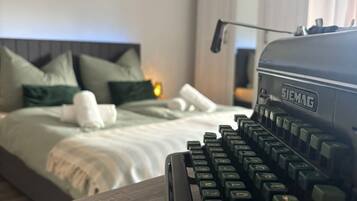 Una máquina de escribir antigua sobre una mesa de madera en una habitación de hotel con cama, almohadas y mesita de noche.