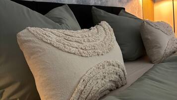 A bed with a textured white pillow and a green blanket in a room with a textured wall and a floor lamp.