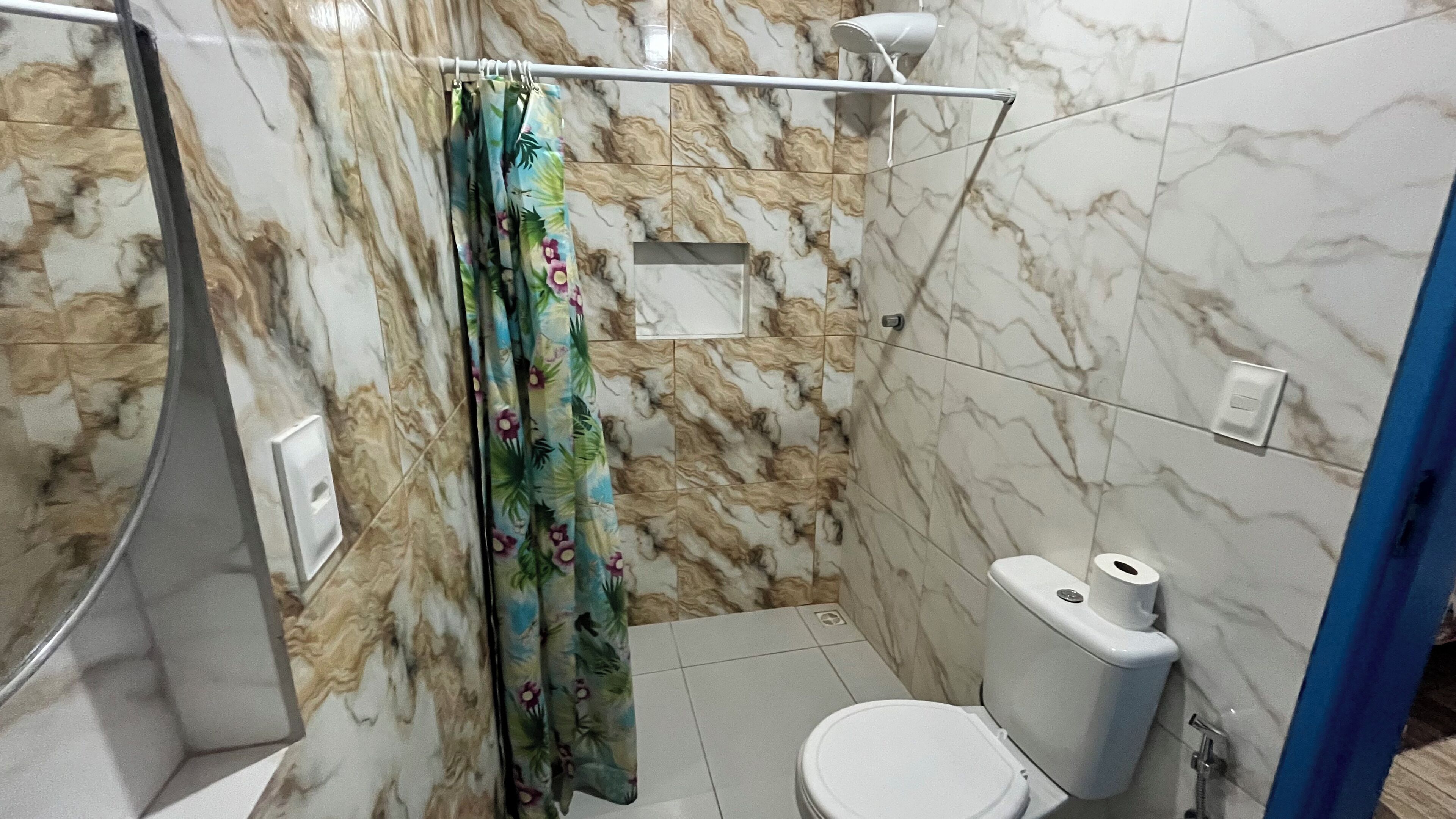 A bathroom with a shower, toilet, and a marble wall.