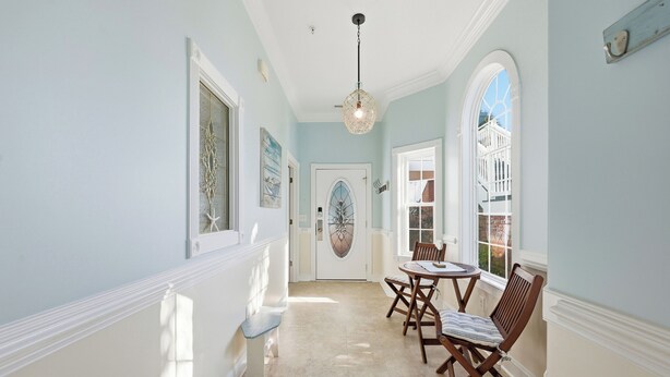 A hallway with a dining area, featuring a white door with a decorative glass panel, wooden chairs, and a hanging light fixture. - AVF 102-101 Spacious 4BR Condo w/ Pool Access – Avian Forest 102-101 (Pawleys Island)