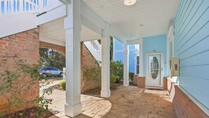 A covered porch with a brick wall and a blue siding house. - AVF 102-101 Spacious 4BR Condo w/ Pool Access – Avian Forest 102-101 (Pawleys Island)
