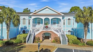 A two-story building with a central entrance, a balcony with a railing, and a staircase leading to the entrance. - AVF 102-101 Spacious 4BR Condo w/ Pool Access – Avian Forest 102-101 (Pawleys Island)