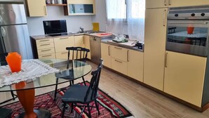 Una cocina compacta con una mesa de vidrio, sillas y un refrigerador.