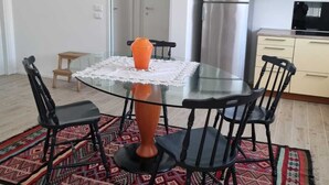 Un comedor con una mesa de vidrio, cuatro sillas, un tapete estampado, un refrigerador y un microondas al fondo.