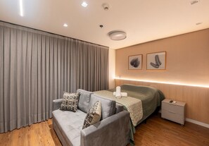 A modern bedroom with a sofa, a bed, a nightstand, and a wall-mounted light. - Glass Art 96 (São Paulo)