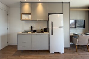 A modern kitchen with a built-in microwave, refrigerator, and a dining area with a TV. - Glass Art 96 (São Paulo)