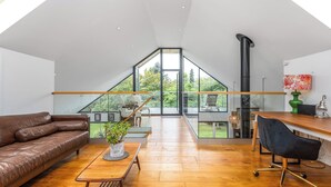 Ein geräumiger Loft mit hoher Decke, einem großen Fenster, Holzboden, einem Ledersofa, einem Esstisch und einem schwarzen Stuhl.
