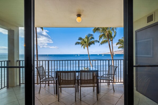 Un balcon avec une table et des chaises, offrant une vue sur la côte, avec des palmiers et la mer.