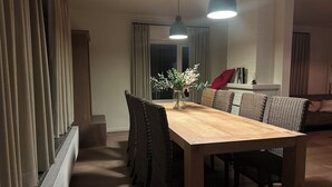 A dining area with a wooden table and wicker chairs, a vase with flowers, and a red cushion on a sofa. - Family-friendly and cozy guesthouse on the edge of the forest. (Kasterlee)