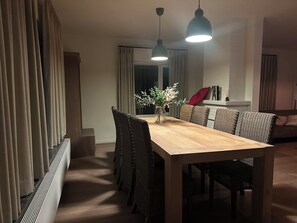 A dining area with a wooden table and wicker chairs, a vase with flowers, and a red cushion on a sofa. - Family-friendly and cozy guesthouse on the edge of the forest. (Kasterlee)