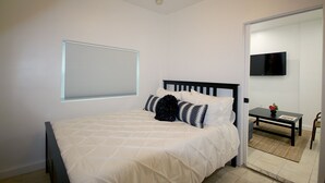A bedroom with a bed, a window with blinds, a bedside table with a flower vase, and a television on the wall. - Historical Little Havana 2/1 Apartment with Parking (Miami)