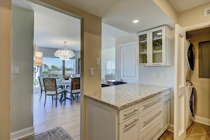 A modern kitchen with white cabinetry, a marble countertop, and a view of the dining area. - 512 Shorewood - Oceanfront Penthouse Retreat with Unbeatable Beach Views (Hilton Head Island)