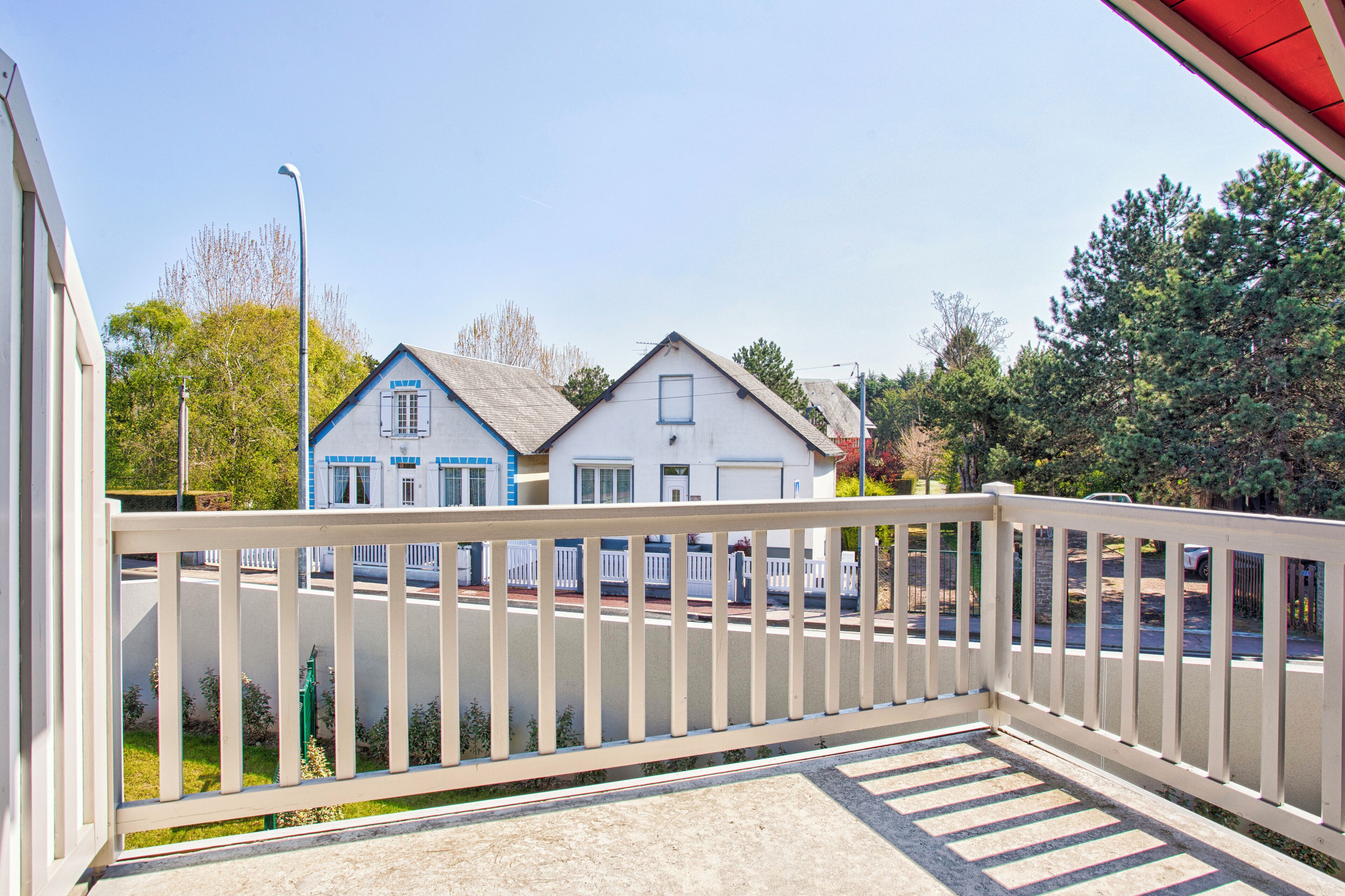 Een balkon met een witte reling, uitzicht op een straat met huizen en bomen.