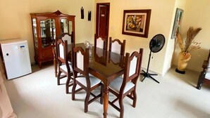 A dining area with a glass-top table surrounded by chairs, a small refrigerator, a fan, and a cabinet. - Imperdível: Incrível casa a 65m da praia do Meaípe (Guarapari)