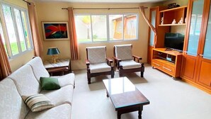 A living room with a sofa, two armchairs, a coffee table, a TV stand, and a painting on the wall. - Imperdível: Incrível casa a 65m da praia do Meaípe (Guarapari)