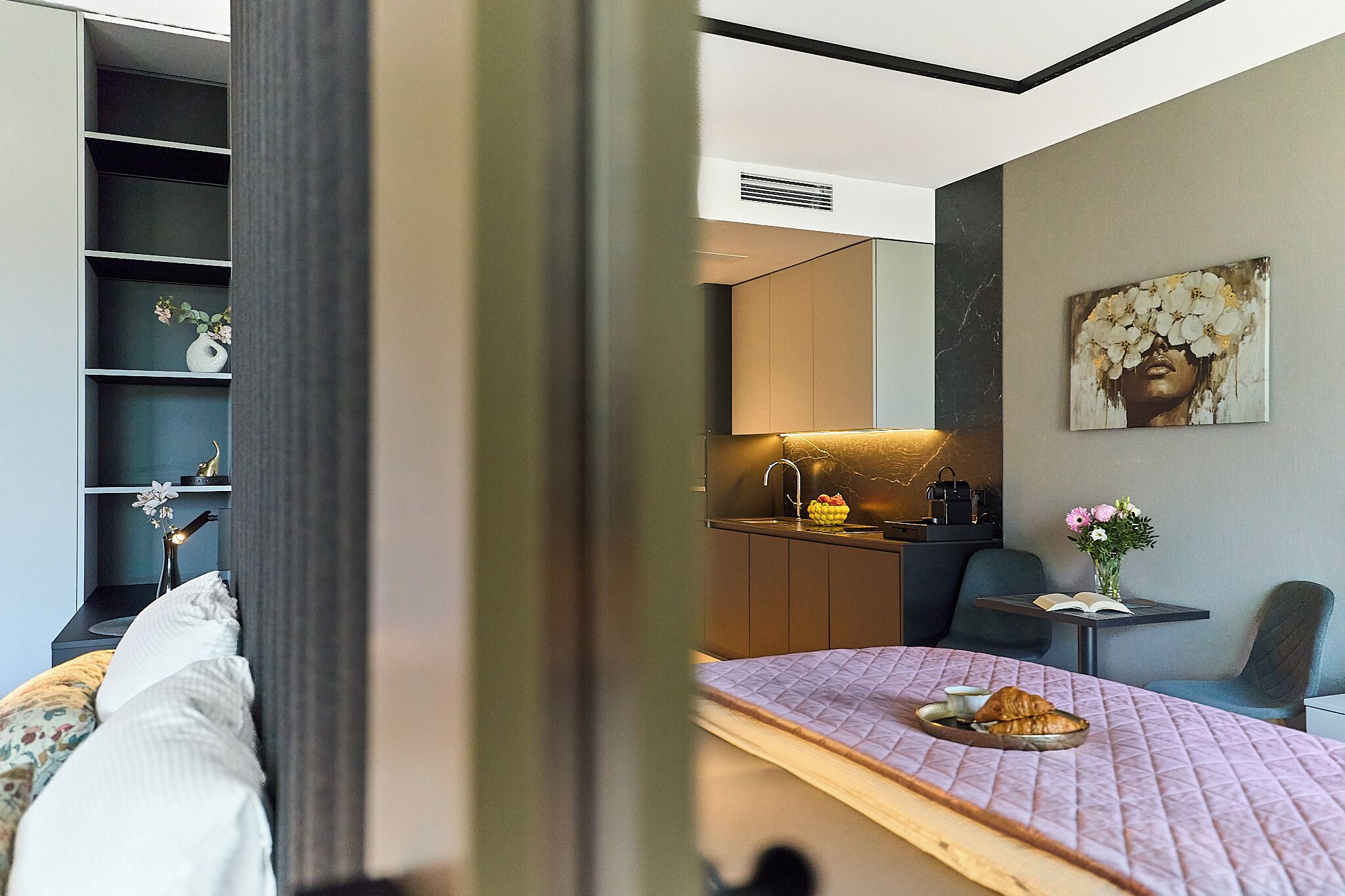 Una habitación de hotel moderna con cama, kitchenette pequeña, zona de comedor y baño.
